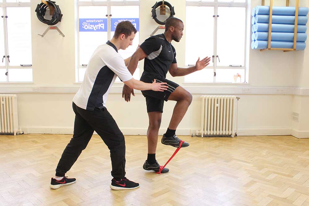 Physiotherapist supervising lower limb exercises using a resistance band.